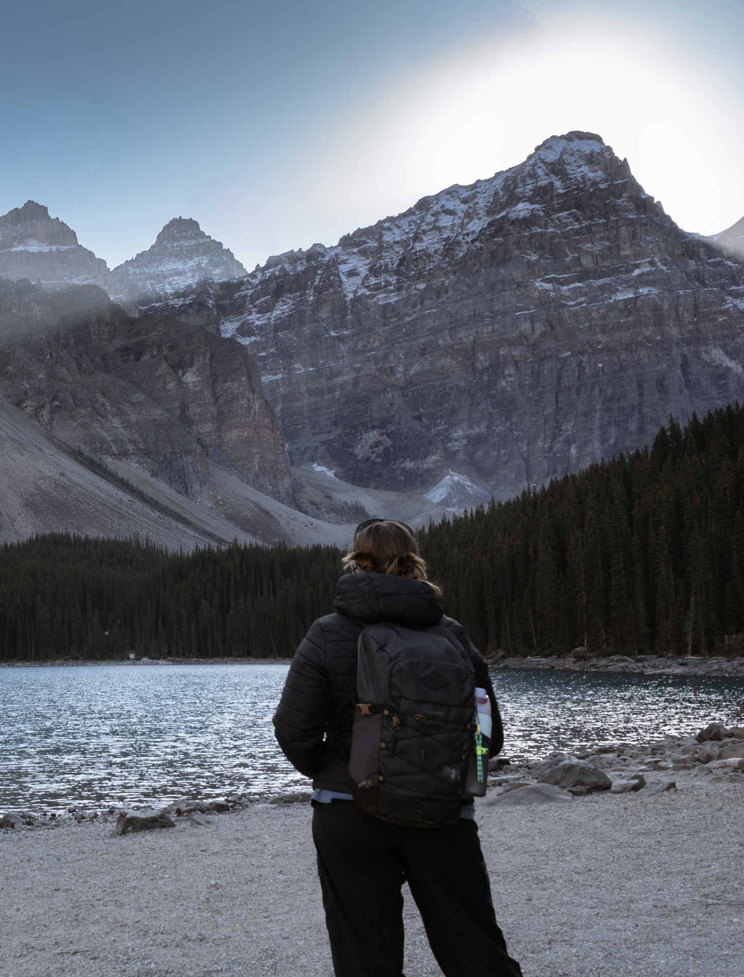 A hiker standing on the shore of Moraine Lake beneath snow-dusted peaks