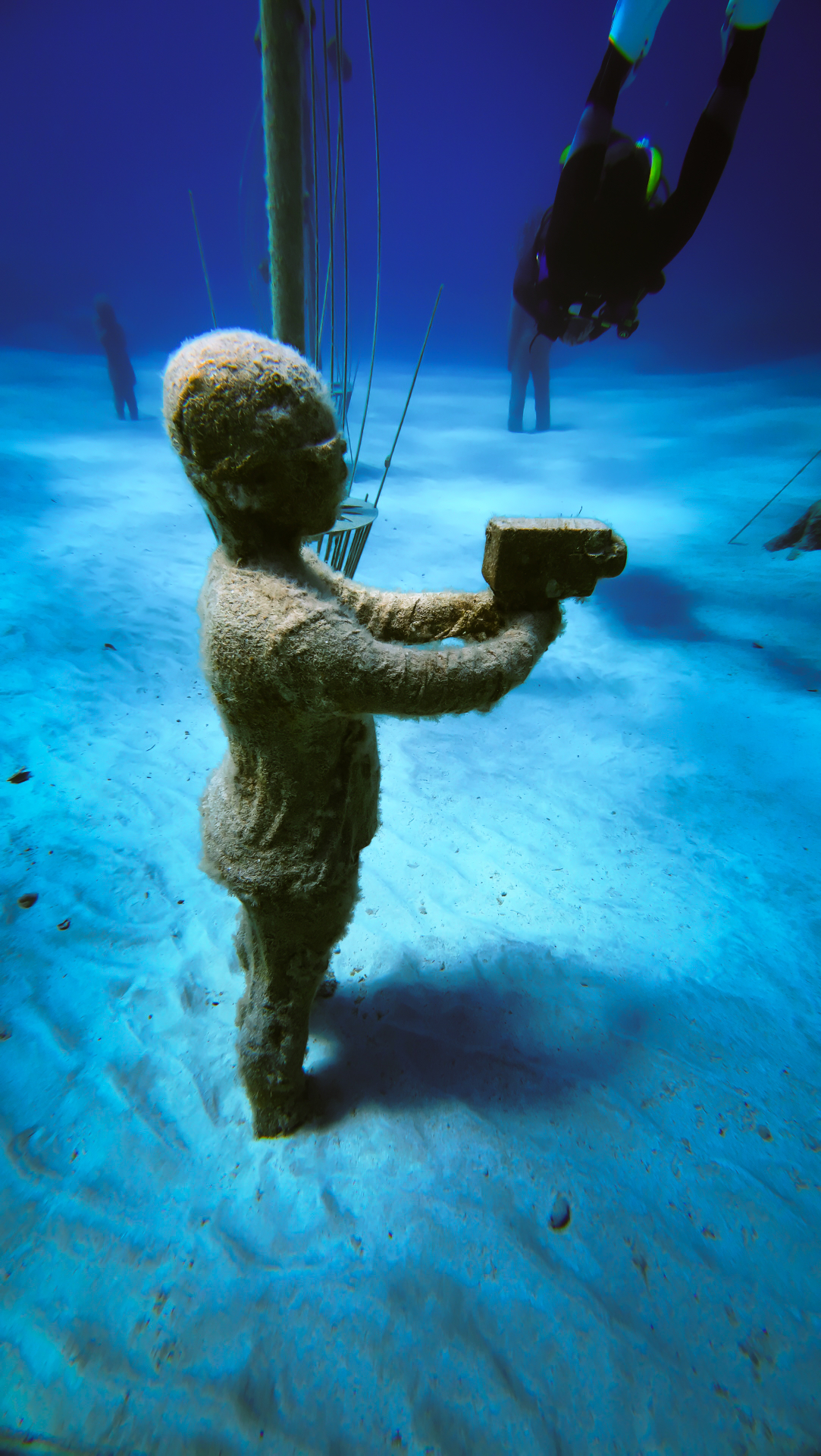 A child sculpture holding a vintage film camera, with a diver hovering above.