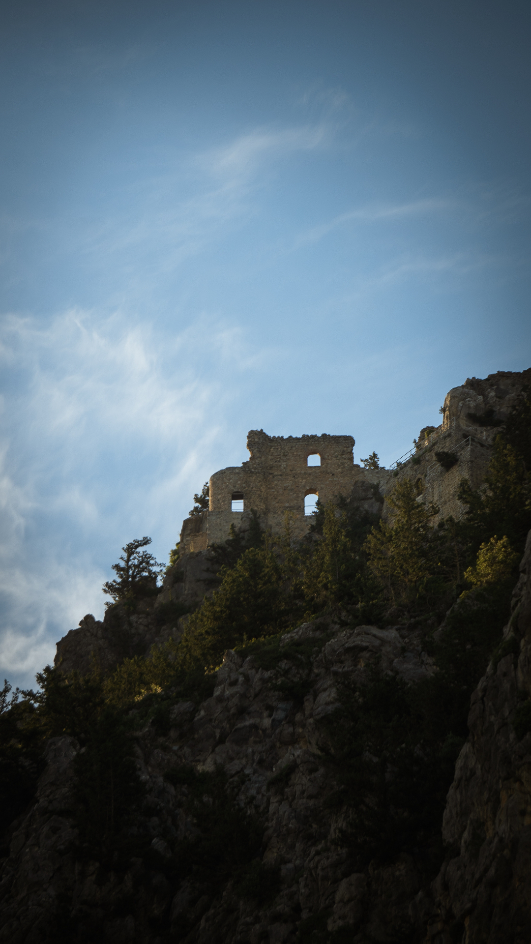 The stone ruins of a crusader castle silhouetted on a jagged peak against a wide blue sky.