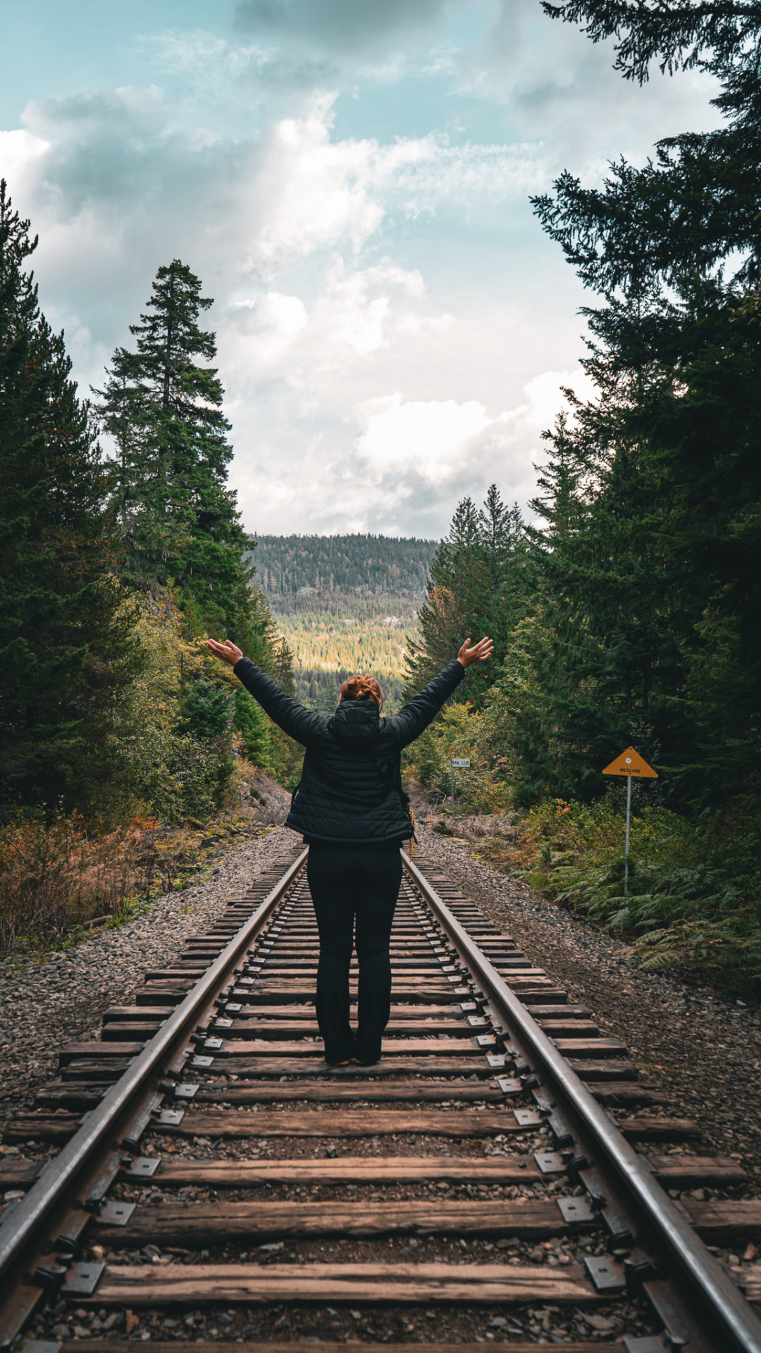 A person standing with arms raised on railway tracks in British Columbia forest.