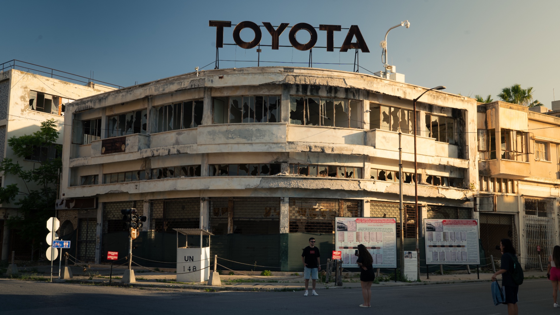 A derelict building crowned by a rusted TOYOTA sign inside the abandoned quarter of Varosha, with a UN marker in the foreground.