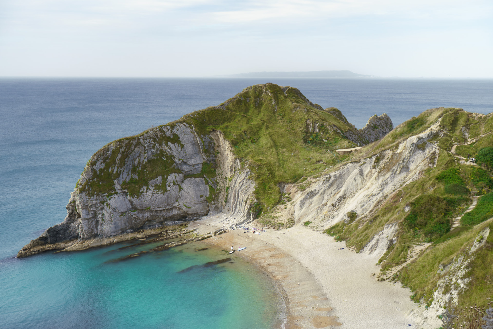 Man O'War Bay with turquoise water and a pebble beach below green cliffs.
