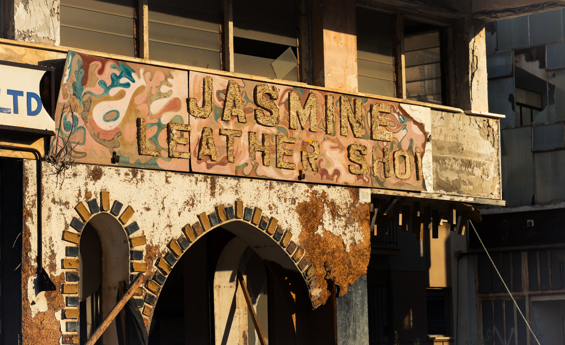 A weathered hand-painted sign reading ‘Jasmine Leather Shop’ above the arched doorway of an abandoned storefront.